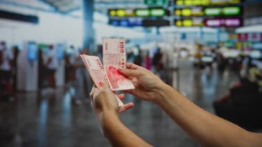Havaalanı terminalinde içi bulanık yolcular ve renkli tabelalarla dolu Tayvan dolarlarını elinde tutan adam, kapalı bir alanda seyahat, iş ve uluslararası finansmanı simgeliyor..