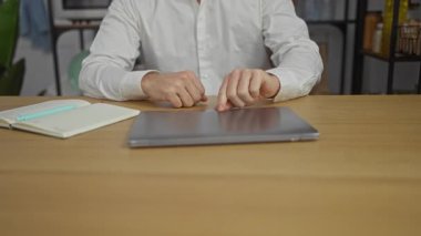 Modern ofis ortamında dizüstü bilgisayarda çalışan, arka planda raflar ve bitkiler olan olgun, beyaz bir adam.