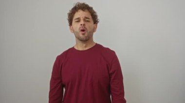 Genç İspanyol bir adam kendine güvenen bir tişörtle dikiliyor, şaşırmış bir ifadeyle normal parmaklarından bakıyor ve izole edilmiş beyaz bir arkaplanda şok olmuş bir yüz görüyor.
