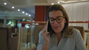 Lüks bir barda telefonda konuşan İspanyol bir kadın, parlak ışık altında gülümsediğini, kapalı alanda bir şehir zarafeti yakaladığını gösteriyor..