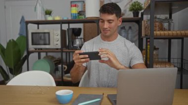 Modern ofis ortamında telefon kullanan genç adam dizüstü bilgisayarlar, bitkiler ve kahve fincanlarıyla çevrili. Teknolojiden anlayan ve rahat bir çalışma ortamı olduğunu gösteriyor..