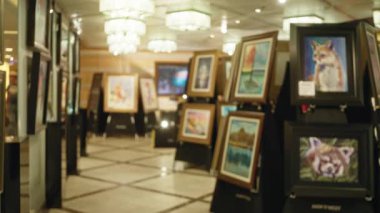 Çerçevelerinde bulanık resimler ve yumuşak ışıklandırma olan sanat galerisi, bir sanat sergisi veya açık artırma önizlemesi için sıcak ve davetkar bir atmosfer sunuyor.
