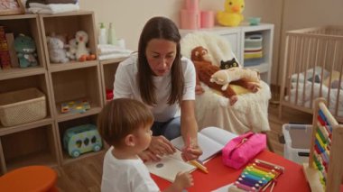 Renkli bir anaokulunda oyuncaklar ve kitaplarla genç bir çocuğa öğretmenlik yapan bir kadın, ev ortamında öğrenme ve yaratıcılığı geliştiriyor..
