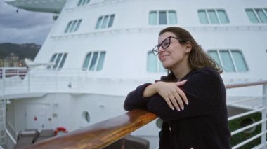 Gözlüklü ve süveter giyen genç İspanyol kadın rıhtımdaki korkuluklara yaslanarak huzurlu bir anın tadını çıkarıyor..