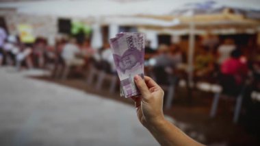 Endonezya Rupiah 'ı elinde tutan eller açık havada kalabalık bir kahve dükkanında para ve ticari işlemler ayarlıyor..