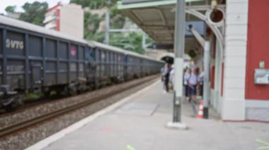 Arka planda yük vagonu olan bir tren istasyonunda odaklanmamış insanlar Bokeh efektli bulanık bir şehir seyahati sahnesi yaratırlar..