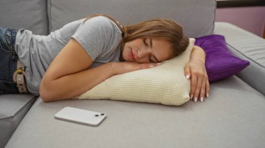 Evdeki kanepede uyuyan bir kadın. Yastık ve akıllı telefon yanında. Ev ortamında rahatlık ve rahatlık göstergesi..