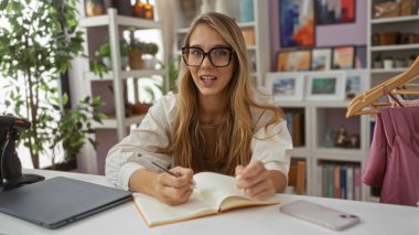 İç dekorasyonda deftere sarı saç ve gözlük takan genç bir kadın..