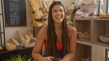 Fırında gülümseyen genç bir kadın. Etrafı ekmek ve hamur işleriyle çevrili.