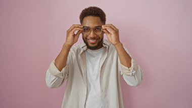 Yakışıklı, Afro-Amerikan bir adam pembe arka plan duvarından izole bir şekilde gülümserken gözlüklerini ayarlıyor.