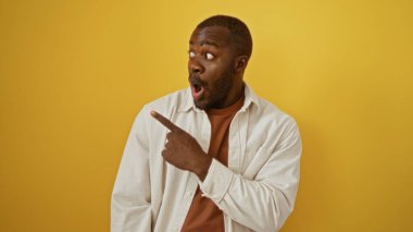 Genç adam, izole edilmiş sarı arka planda hayret verici bir ifadeyle çekici ve yakışıklı bir erkeği sürpriz bir anda yakalıyor.