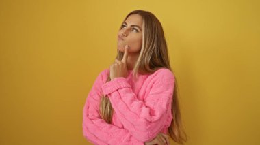 Parlak sarı bir duvara karşı düşünen pembe bir kazak giyen düşünceli bir kadın..