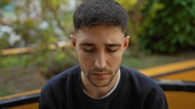 Şehir parkında gözleri kapalı genç bir adam açık havada yemyeşil bir alanda huzurlu bir ifade sergiliyor..