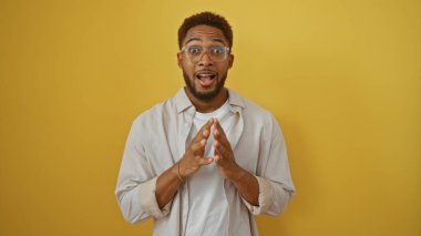 Gözlüklü ve sakallı genç adam izole edilmiş sarı bir arka planın önünde şaşkın şaşkın bakıyor.