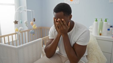 Genç adam elleri yatak odasında, bebek beşiğinin yanında, yatakta oturuyor. Ev ortamındaki stresi yansıtıyor. Evdeki kaygılarını ve düşüncelerini gösteriyor..