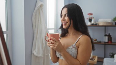 Rahatlatıcı bir spa odasında çay içen, esmer saçlı ve dantelli bir bluz giyen genç bir kadın.