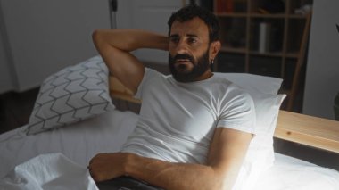 Yakışıklı, sakallı, evde rahat bir yatak odasında dalgın dalgın yatan bir İspanyol.