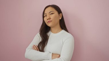 Pembe bir duvara yaslanmış, beyaz bir kazak giymiş sakin bir ifade ve uzun saçlar sergileyen bir kadın..