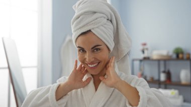 Güzeller güzeli bir kadın, bir sağlık merkezinde, kafasında bir havluyla, bir salonun içinde sıcacık bir gülümsemeyle, spa gününün tadını çıkarıyor.