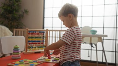 Çocuk parlak bir anaokulu ortamında eğitici oyuncaklarla oynuyor, kapalı bir ortamda odak ve öğrenme becerileri gösteriyor.