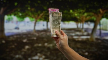 Bir şehir parkında el ele tutuşan Hindistan Rupisi banknotları şehir ortamında iş ve finans kavramlarını resmediyor..