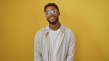 Yakışıklı, Afro-Amerikalı, parlak sarı arka planda gülümseyen, gözlüklü ve günlük kıyafetli bir adam.