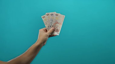 Elinde Türk lira banknotları tutan bir adamın eli mavi arka plan duvarında izole edilmiş, finans ve döviz konseptini vurguluyor..