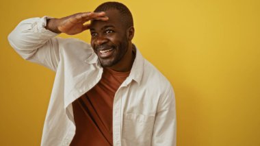 Afro-Amerikalı bir adam gülümsüyor ve parlak sarı bir arka plana el ele bakıyor..