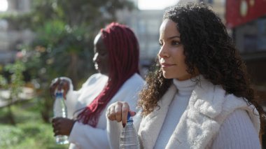 Dışarıda elinde su şişeleriyle duran kadınlar, bir Afrikalı ve bir melez arkadaş, güneşli havalarda şehir parkının keyfini çıkarıyorlar, arkadaşlığı ve eğlenceyi yakalıyorlar..