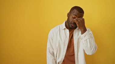 Gözleri ovalayan genç adam izole edilmiş sarı arka planda yorgun..