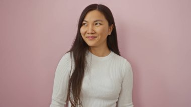 Pembe duvarın önünde güvenle gülümseyen, beyaz bir kazak giyen, Asyalı güzelliğini ve çekiciliğini sergileyen, gençlik zarafetini ve modernliğini sembolize eden bir kadın..