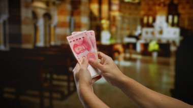 Kilisede Çin Yuanı banknotları tutan adam, finans ve maneviyatın kesişimini parlak, odaklanmış aydınlatma ve mimari detaylarla vurguluyor..