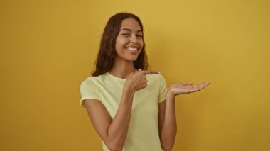 Sarı arka planda tek başına duran bir kadın gülümseyip avuç içini işaret ediyor.
