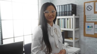 Zarif bluzlu kadın, modern ofis ortamında, raflar ve belgelerle, profesyonel ve şık tavırlar sergiliyor..