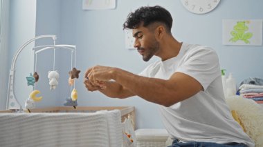 Genç İspanyol adam beşikteki bebeğin fotoğrafını çekiyor rahat yatak odası ortamında yumuşak ışıklandırmalı akıllı telefon kullanıyor..