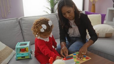 Anne ve kızı rahat oturma odası ortamında oyuncaklarla oynuyor, sıcak, davetkar bir atmosfer içeren kapalı bir apartman dairesinde aile sevgisini ve yakınlaşmayı ön plana çıkarıyor.