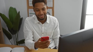 Ofisteki yakışıklı adam masada otururken akıllı telefon ekranına gülümsüyor.