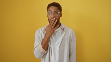 Gözlüklü ve şaşırmış bir ifadeyle izole edilmiş sarı arka planda duran genç bir adam..