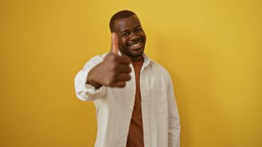 Yakışıklı Afrikalı adam gülümsüyor ve izole edilmiş sarı arka plan için başparmak kaldırıyor.
