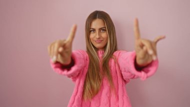 Pembe süveter giyen, neşeli bir ifadeye sahip, parlak pembe bir arkaplanı işaret eden bir kadın..