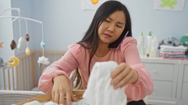 Bebek odasında beşikte meşgul bir anne ile aynı anda birden fazla iş yapan bir kadın Asyalı bir kadının ev içi işlerini dengeliyor.