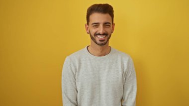 Yakışıklı, İspanyol asıllı, rahat tavırları ve modern saç stiliyle parlak sarı arka planda sırıtan genç bir adam..