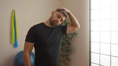 Spor salonunda rahat bir ifadeyle esneyen genç bir İspanyol, doğal ışıklandırma ile sakin bir ortamda fiziksel zindelik ve farkındalık sergiliyor..