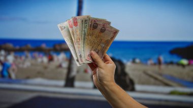 Güneşli bir sahil arka planında Emirati Dirhams 'ı tutan insanlar deniz kenarında eğleniyor, para, iş ve uae' deki açık hava aktivitelerini vurguluyorlar..