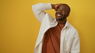 Sarı bir arka planda gülümseyen, rahat tavırlı yakışıklı Afro-Amerikan bir adam.