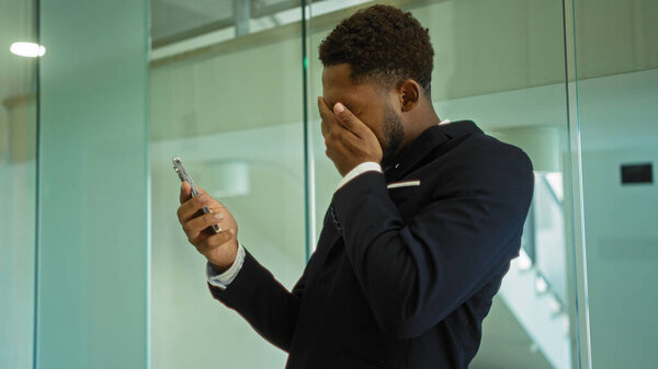 Young man in office looking at phone covering face indoors with glass background
