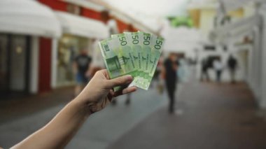 Elele tutuşan Norveçli kronlar, bulanık yayalar ve kentsel zemin ile işlek bir şehir caddesinde, modern ekonomik temaları ve kentsel yaşam tarzını yakalayan açık hava banknotları oluşturuyor..