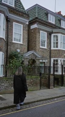 Chelsea Londra 'daki büyüleyici tuğlalı evlerin önünden geçen bir kadın. Sessiz bir sokak köşesinde yemyeşil ve geleneksel mimarisi olan..