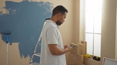 Yeni dairenin oturma odasında akıllı telefon kullanan İspanyol bir adam yenileme projesi sırasında kutularla çevrili..