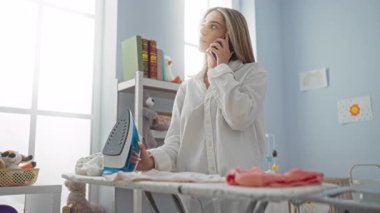Çamaşırhanede telefonda konuşurken ütü yapan kadın. Ütü masası ve oyuncaklarla..